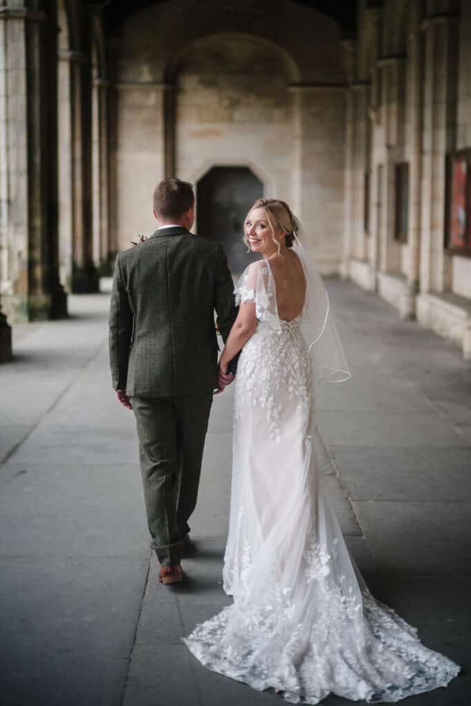 Bride looks over her shoulder whilst walking with Groom outside St Salvator's in St Andrews