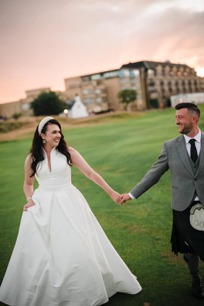 Bride and groom walk hand in hand with the Old Course Hotel behind them