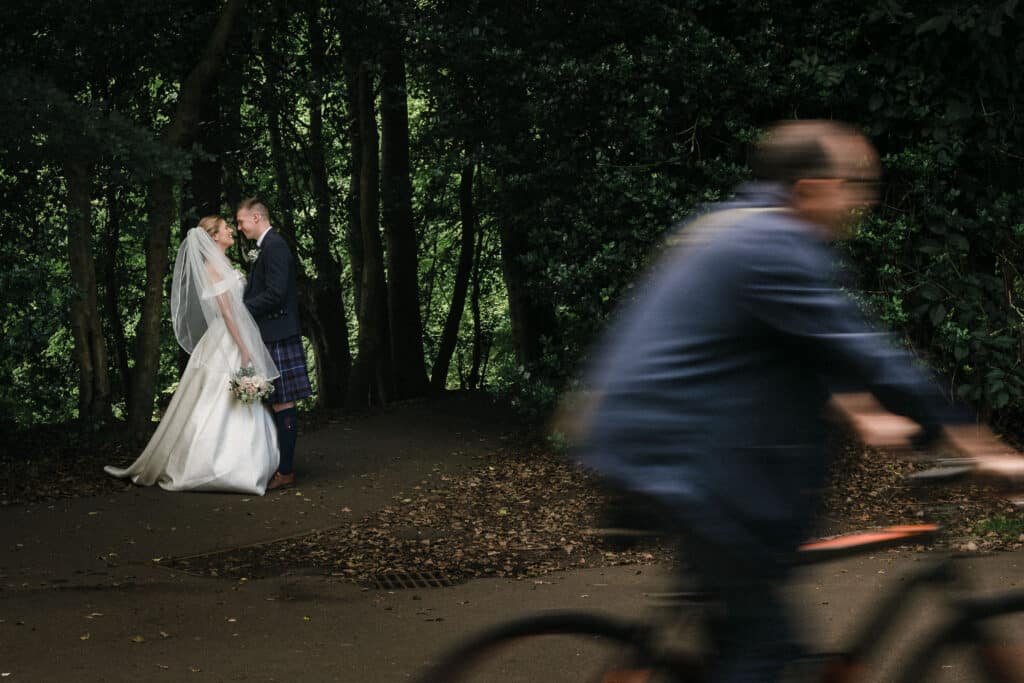 A cyclist zooms past a bride and groom in Pollok Park