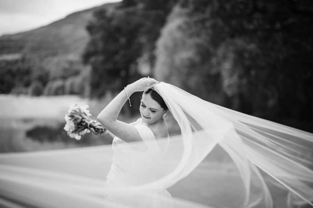 B&W image of a bride holding onto her veil during her Loch Lomond Wedding