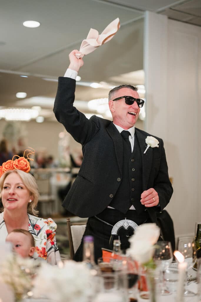 Father of the bride wears sunglasses and waves napkin at Old Course Hotel
