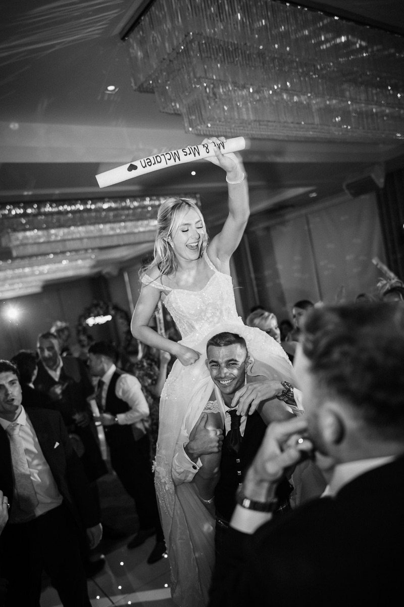 A bride dances whilst being hoisted on someone's shoulders at Lochside House Hotel