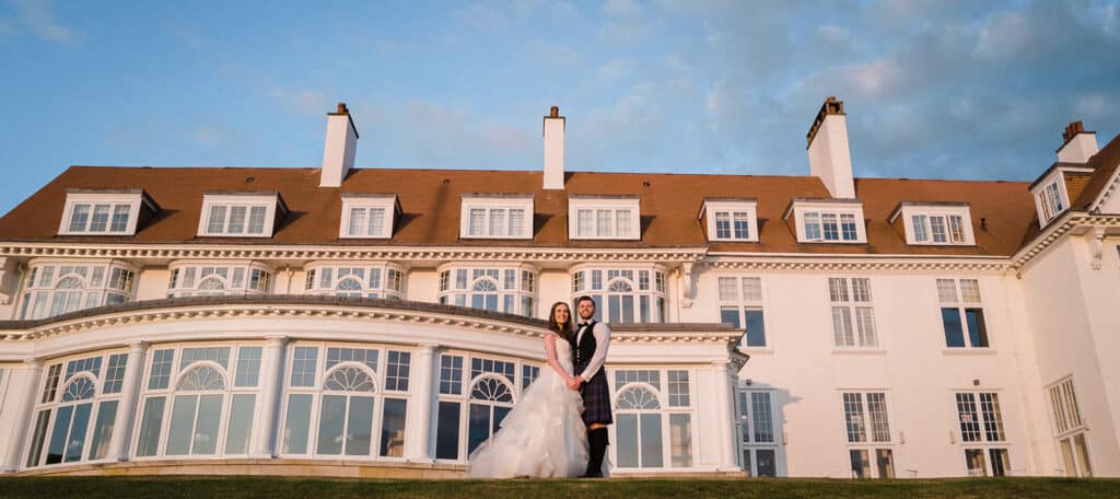Bride and Groom stand outside Trump Turnberry in Ayrshire during golden hour