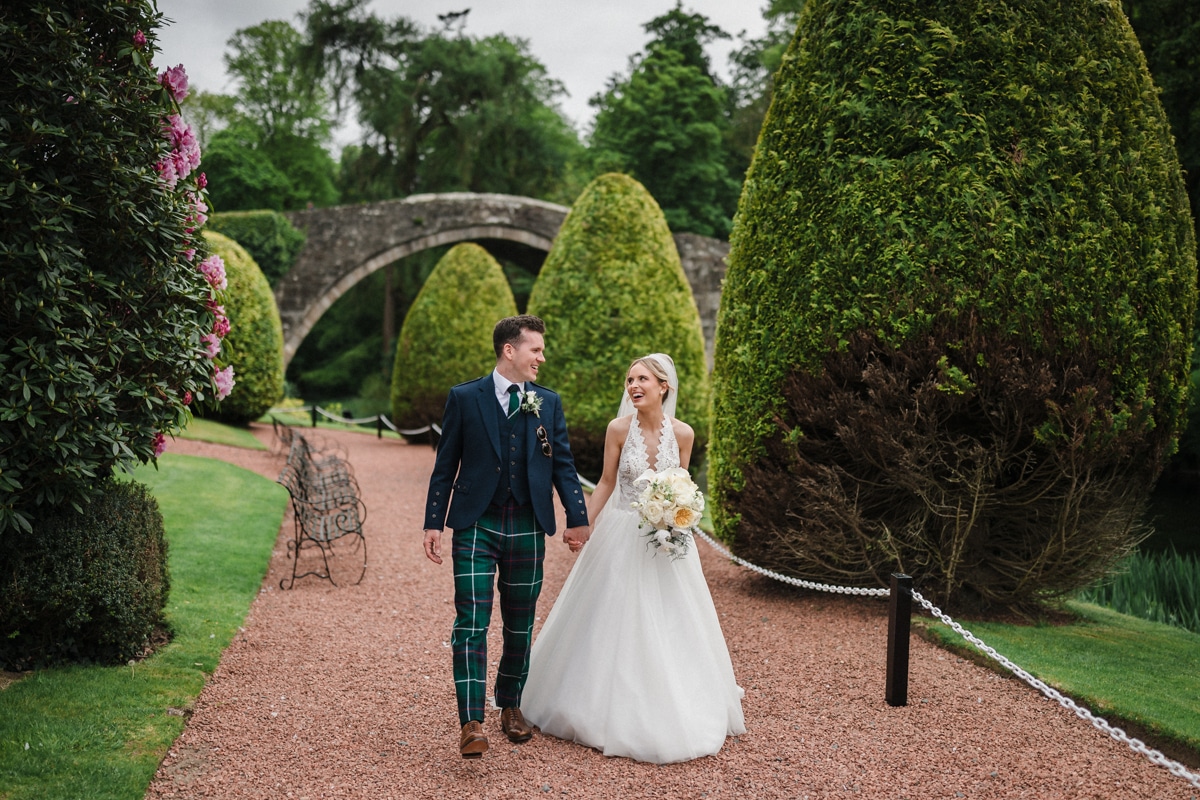 Bride and Groom walk smiling at each other, the famous Brig at Brig o'dion behind them